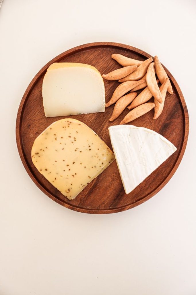 Assorted cheeses and breadsticks on a wooden board, perfect for gourmet presentation.