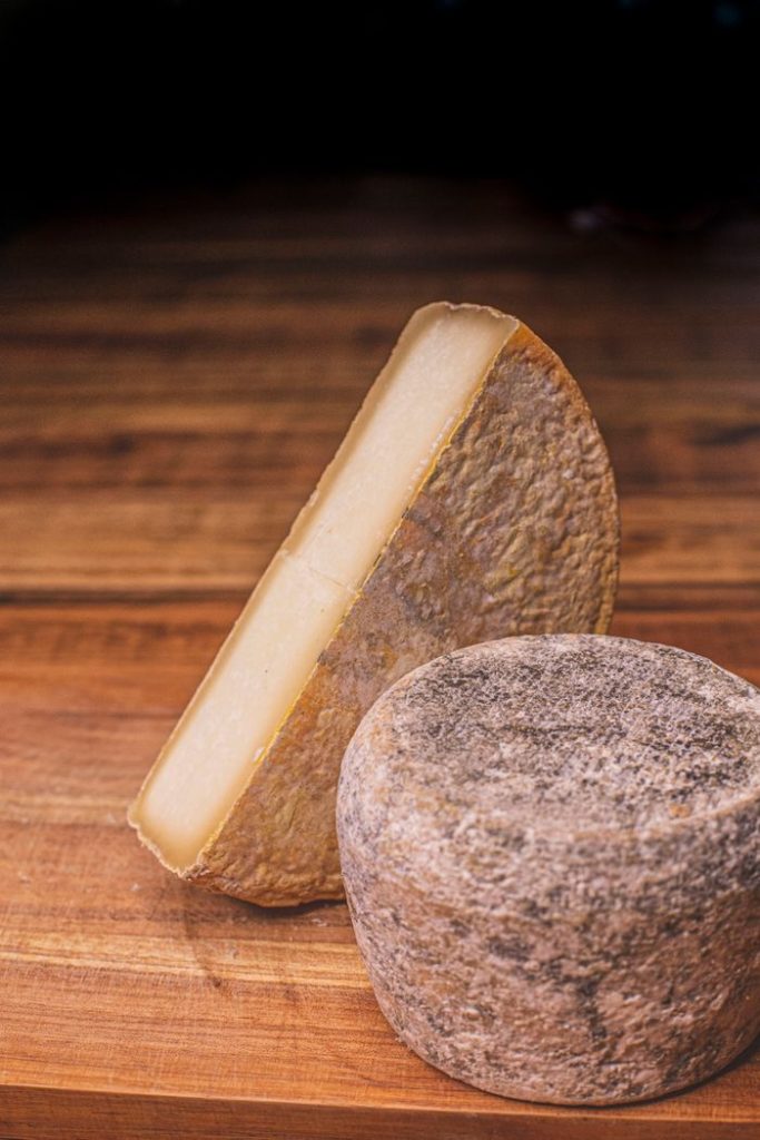 Close-up of artisanal cheese on a wooden board in a kitchen setting, showcasing texture and detail.